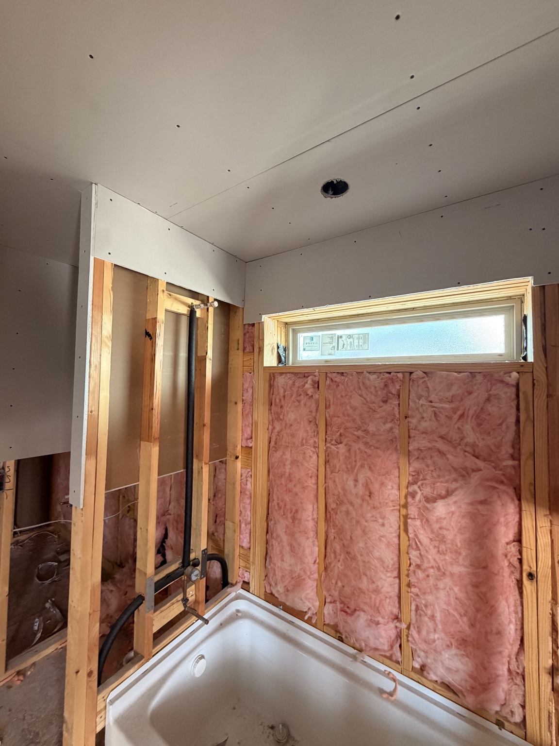 Drywall installation underway around a bathroom tub